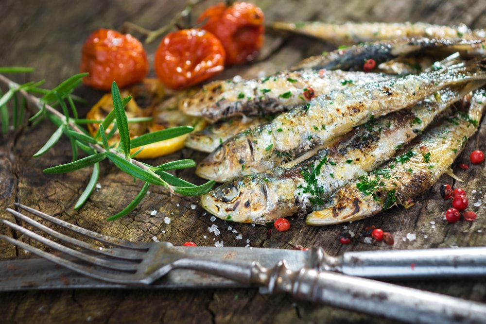 grilled sardines with tomatoes and herbs next to a fork and a knife served in our gourmet food tours in Lisbon at Treasures of Lisboa